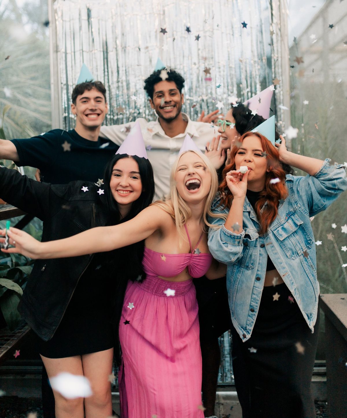 Friends in party hats cheering under falling confetti at a birthday party